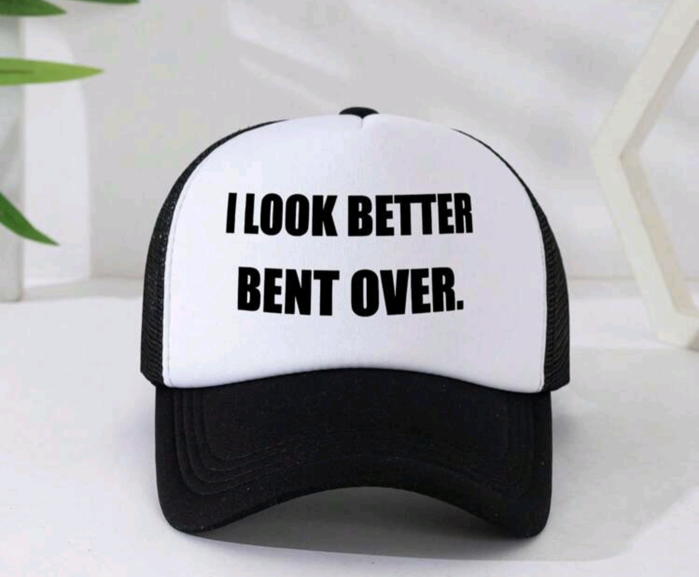 Black and white mesh trucker hat with the bold adult humor text "I LOOK BETTER BENT OVER" printed on the white foam front panel. Ideal novelty gag gift for stag parties and student nights.